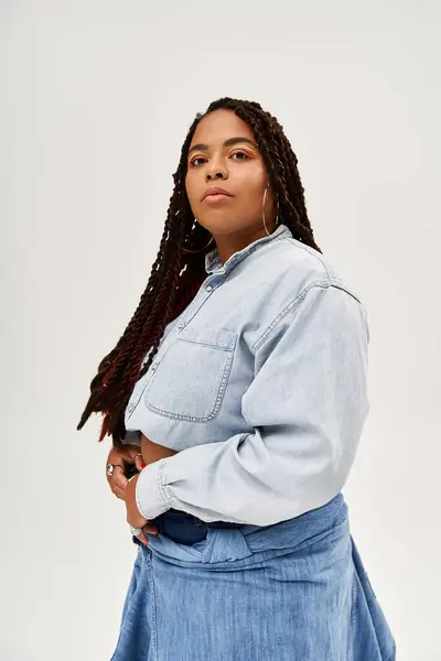 Uma mulher Africano-Americana confiante posa em uma camisa jeans e saia contra um pano de fundo cinza. — Fotografia de Stock