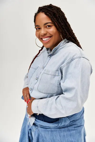 A stylish African American woman in braids poses in a denim outfit on a grey backdrop. — Stock Photo