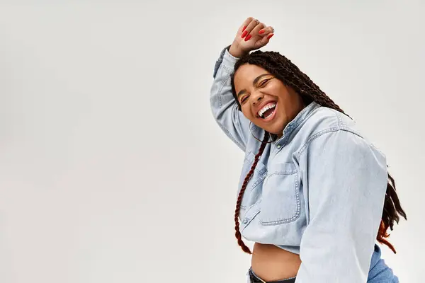 Una vibrante donna afroamericana con trecce posa gioiosamente in denim, trasudando fiducia e beatitudine. — Foto stock