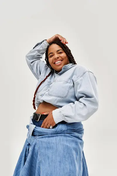 Una donna afroamericana allegra con i capelli intrecciati mette in mostra il suo stile denim in uno studio. — Foto stock