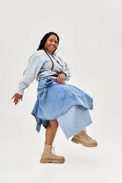 A pretty woman with braids showcases her denim outfit while striking a playful pose in the studio. — Stock Photo