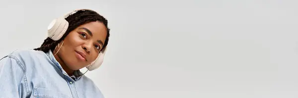 Una gioiosa donna afroamericana in trecce posa in un abito di jeans su uno sfondo grigio, striscione — Foto stock