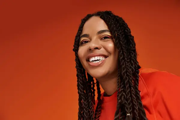 A vibrant woman showcases her stylish casual outfit while posing joyfully on an orange background. — Stock Photo