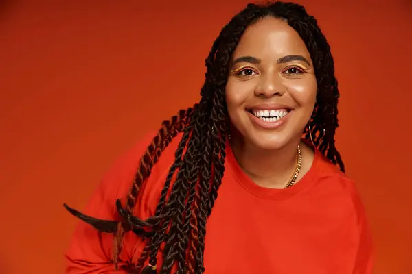 A joyful African American woman in a stylish outfit radiates positivity against an orange backdrop. — Stock Photo