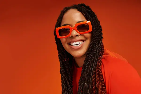 A stylish African American woman with braids smiles confidently, showcasing her bright fashion. — Stock Photo