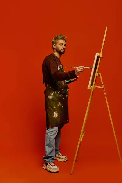 A handsome young man in casual attire expresses his artistic flair while painting at an easel. — Stock Photo