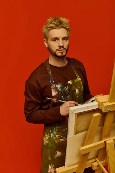 Hombre guapo vestido con un delantal está a punto con pincel en la mano, listo para crear arte. - foto de stock