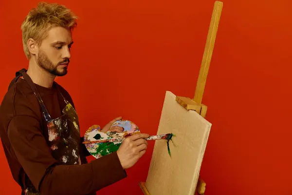 Joven creativo pinta hábilmente sobre un lienzo en blanco sobre un llamativo fondo naranja. - foto de stock