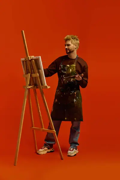 Handsome young man creates art on a canvas while wearing an artists apron and smiling warmly. — Stock Photo