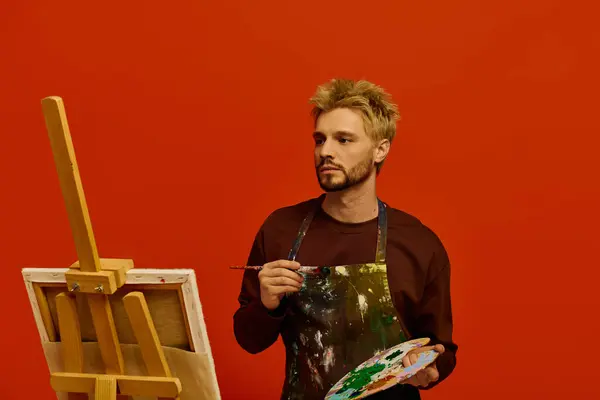 A young artist thoughtfully holds a palette, creating vibrant art in his studio. — Stock Photo