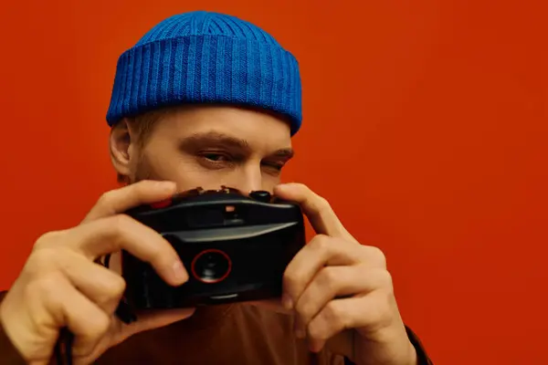A handsome young man in a blue beanie focuses intently on his camera, ready to capture memories. — Stock Photo