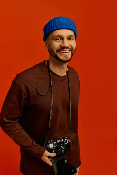 Charming young man smiles while holding a vintage camera in a lively studio environment. — Stock Photo