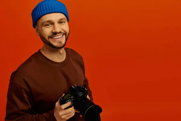 Un giovane allegro con un berretto blu tiene una macchina fotografica, irradiando gioia in un ambiente vivido. — Foto stock