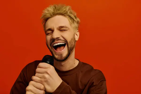 Un bel giovanotto canta allegramente tenendo in mano un microfono e sorridendo brillantemente. — Foto stock