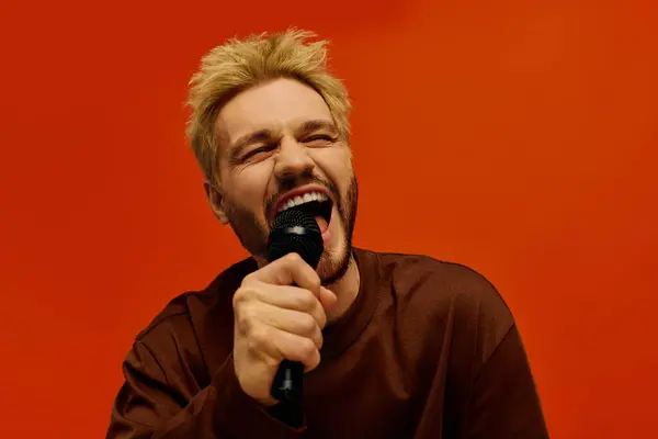Bel giovanotto canta appassionatamente, godendo il momento con uno sfondo arancione brillante. — Foto stock