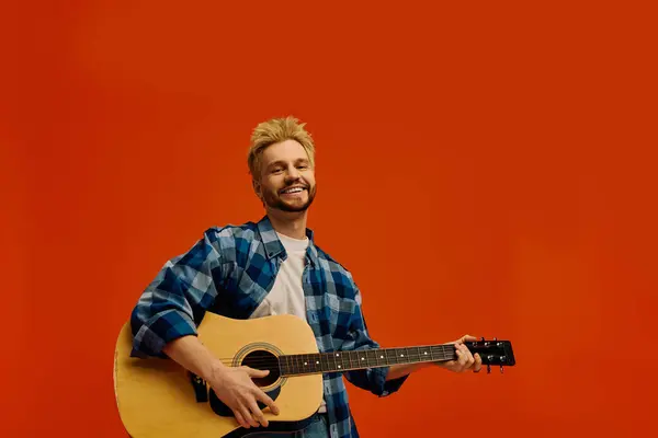 Con un sorriso luminoso, un bel giovanotto si diverte a suonare la chitarra, vestito con disinvoltura. — Foto stock