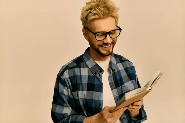 Чарівний молодий чоловік посміхається, коли читає книгу, оточену теплим освітленням і розслабленим вібеєм. — стокове фото