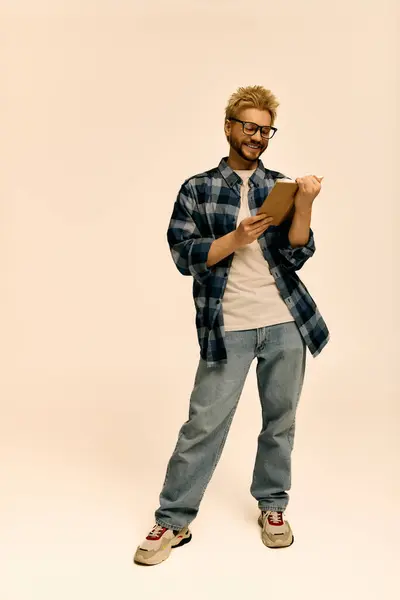 Charmanter junger Mann steht selbstbewusst mit Klemmbrett und sprüht im Atelier vor Kreativität und Freude. — Stockfoto