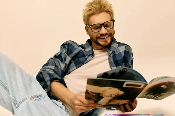 A stylish young man with blonde hair and glasses relaxes while reading a magazine on a cozy day. — Stock Photo