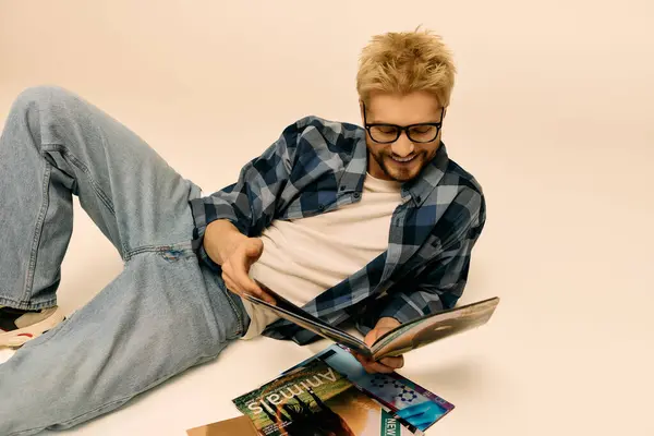 Un bel giovane uomo si trova comodamente sul pavimento, assorto nella lettura di riviste colorate. — Foto stock