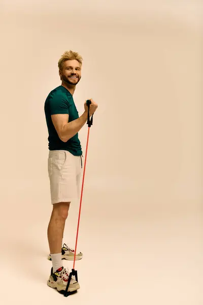 Handsome young man in workout gear performs exercise using resistance band, showcasing strength. — Stock Photo