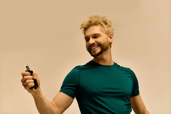 Attractive young man smiles brightly while playfully holding a device in a neutral space. — Stock Photo