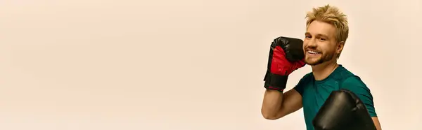 Handsome young man poses with boxing gloves, exuding confidence in a modern workout studio. — Stock Photo