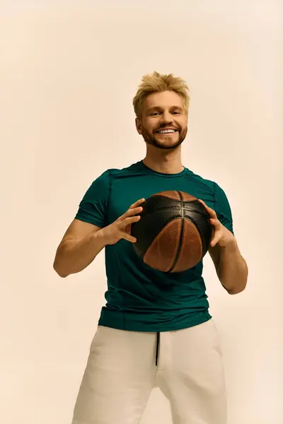 Bello giovane uomo sorride brillantemente mentre tiene in mano una pallacanestro, trasudando fiducia e gioia. — Foto stock