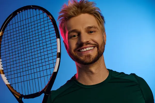 Bello giovane uomo sorride brillantemente mentre tiene una racchetta da tennis su uno sfondo colorato. — Foto stock