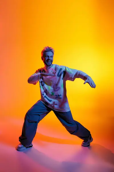 Joven animado realizando movimientos de baile enérgicos rodeados de luces coloridas. - foto de stock
