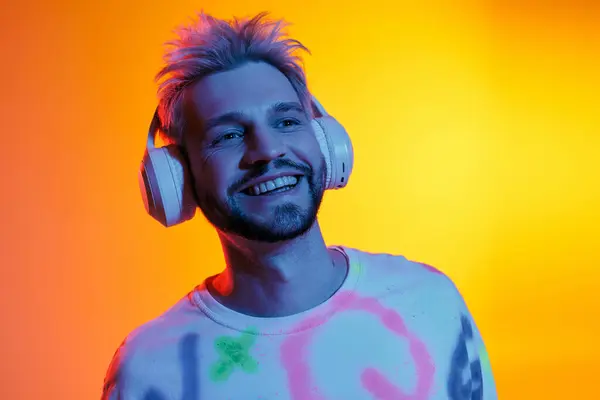 Bello giovane uomo sorride luminoso mentre immerso in colori vivaci e battiti di musica. — Foto stock