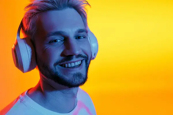 Gioioso giovane uomo si immerge nella musica mentre indossa le cuffie in mezzo a uno sfondo colorato. — Foto stock