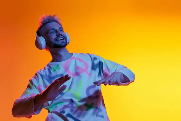 Bel giovanotto con le cuffie danza gioiosamente sotto luminose tonalità al neon, catturando il momento. — Foto stock