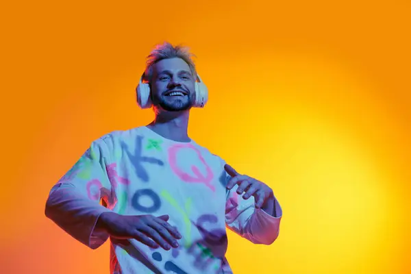 Giovane con un'espressione gioiosa balla alla musica su uno sfondo colorato, indossando cuffie. — Foto stock