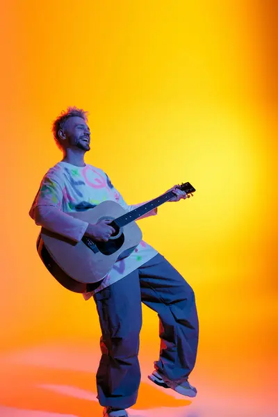 Giovane gioioso suona la chitarra su uno sfondo luminoso, mostrando creatività e passione. — Foto stock