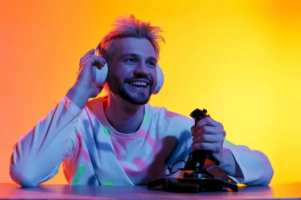 Un bel giovane uomo sorride ampiamente mentre si diverte a giocare, indossando cuffie in un ambiente colorato. — Foto stock