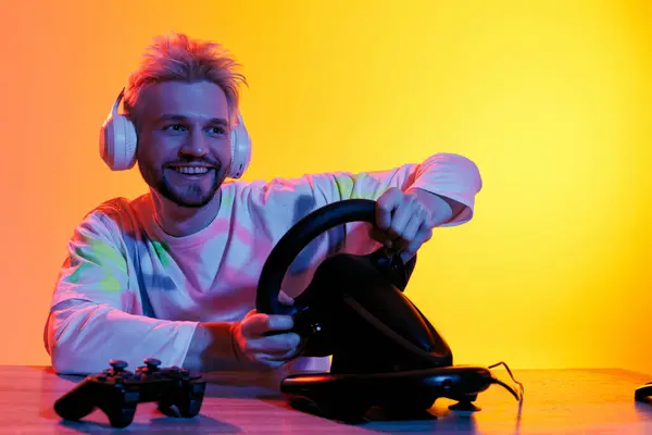 Handsome young man engaged in an exciting gaming session with headphones and a racing wheel. — Stock Photo
