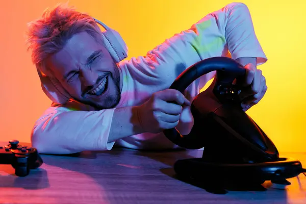 A handsome young man with headphones plays a racing game, showing enthusiasm and concentration. — Stock Photo