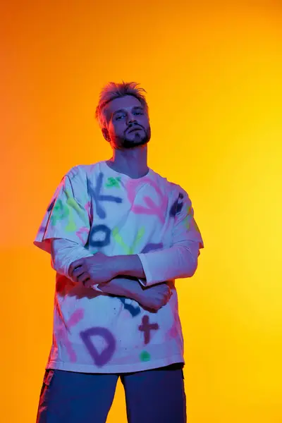A handsome young man stands with crossed arms, showing off his colorful shirt in a bright setting. — Stock Photo