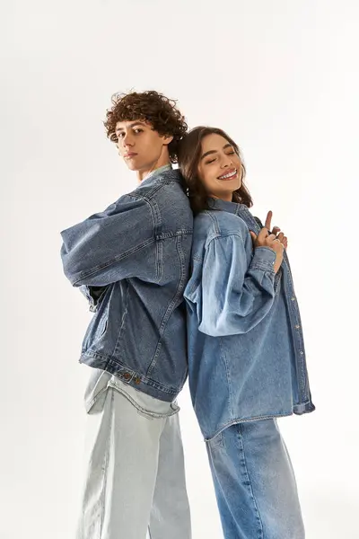 A young couple stands back to back in a trendy studio, smiling in stylish denim. — Stock Photo