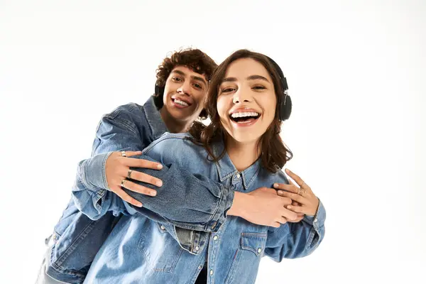 Joyful young couple in matching denim jackets enjoying music and laughter in a bright space. — Stock Photo