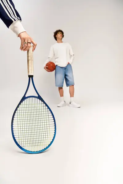 Una joven pareja muestra su amor por los deportes y el estilo con una raqueta de tenis y baloncesto. - foto de stock