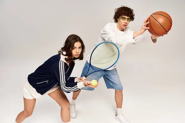 A trendy couple enjoys tennis and basketball gear, showing love and energy in a studio. — Stock Photo