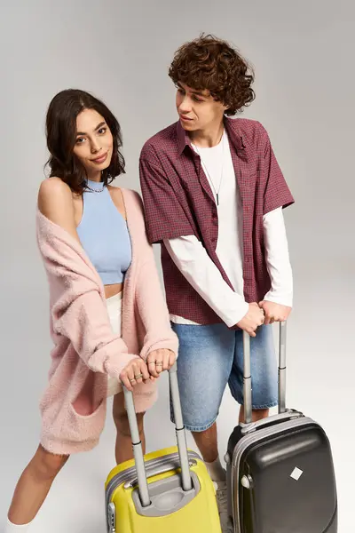 Young couple dressed in trendy outfits stands with suitcases, ready for their romantic getaway. — Stock Photo