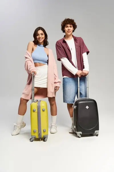 Charming pair smiles while holding vibrant suitcases in a contemporary backdrop, ready to explore. — Stock Photo