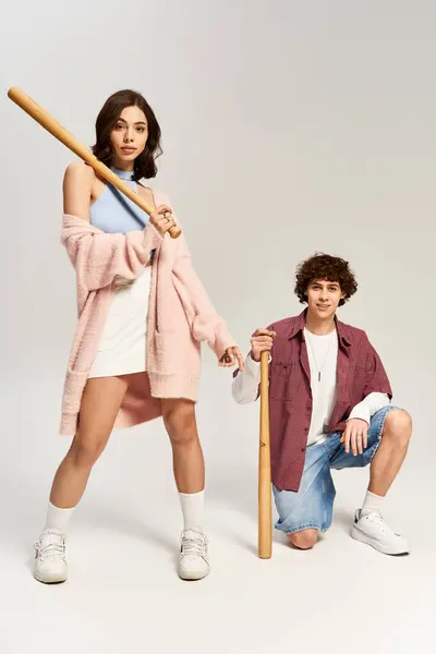 Una elegante pareja joven muestra su espíritu lúdico con murciélagos de béisbol en un estudio de moda. - foto de stock