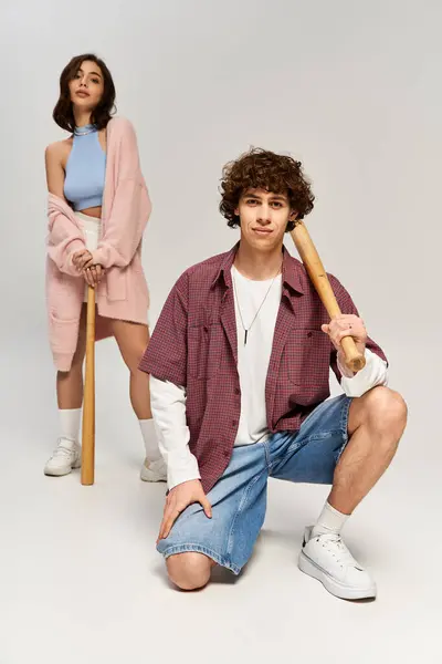 Junges Paar posiert glücklich mit hölzernen Fledermäusen und rockt ihre trendigen Outfits. — Stockfoto