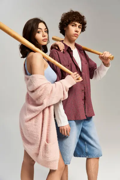 Pareja joven de moda se encuentra junto con los murciélagos de béisbol, mostrando su estilo de moda y el amor. - foto de stock