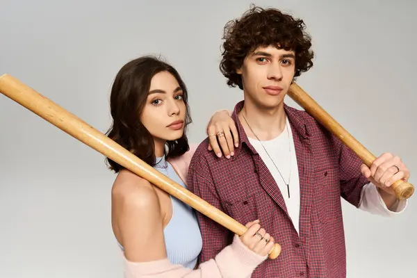 A young couple stands close together, each holding a wooden bat, exuding love and style. — Stock Photo