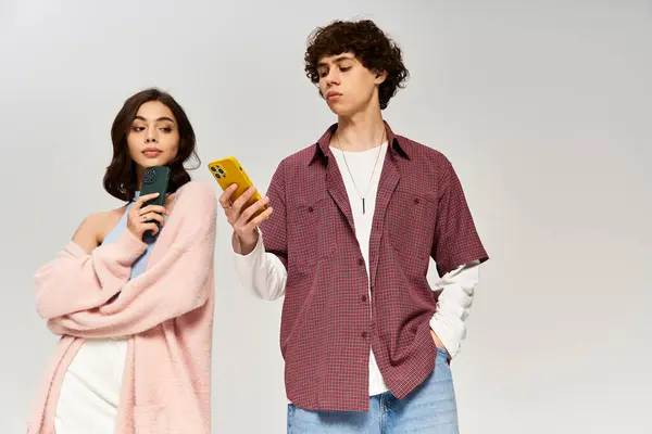 A stylish young couple stands side by side, engaged with their smartphones, radiating love. — Stock Photo